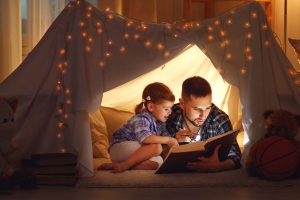 happy family father and child daughter reading a book in tent at home